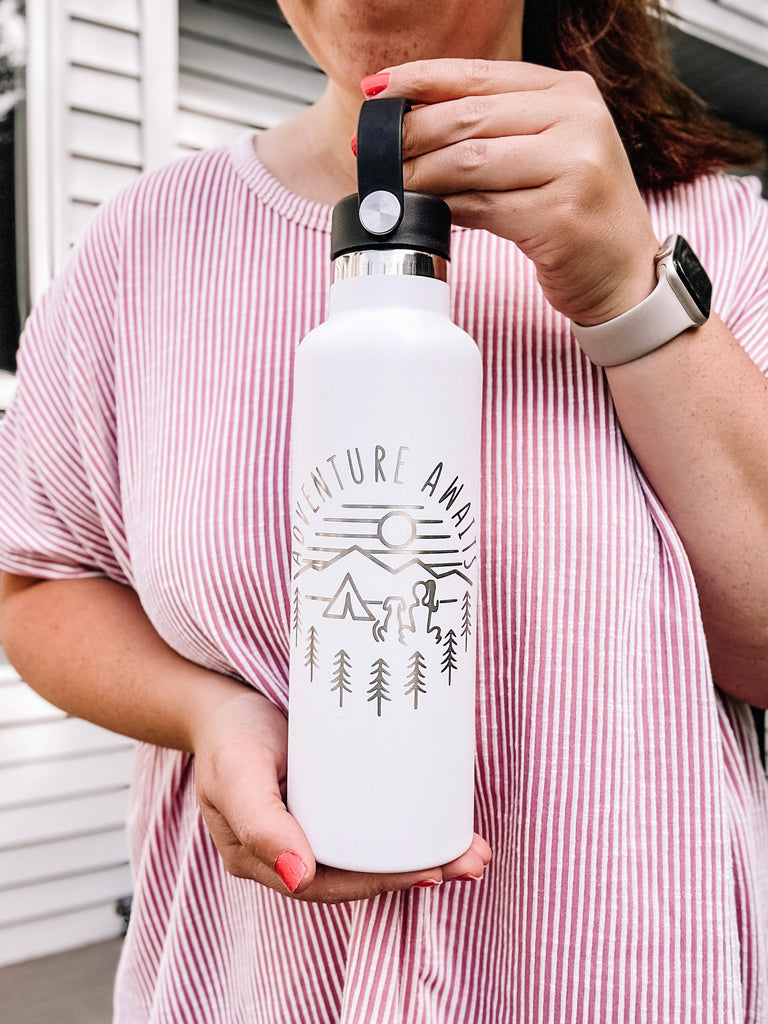 woman holding white water bottle that says adventure awaits