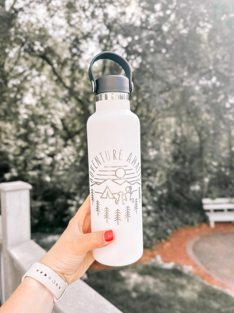 hand holding white water bottle that says adventure awaits